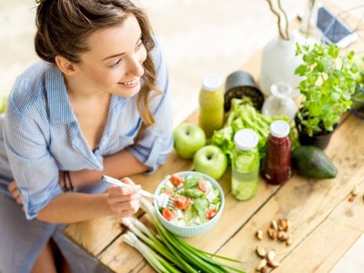 Frau steht an der Küchenarbeitsplatte und isst einen Salat aus einer Bowl. 
