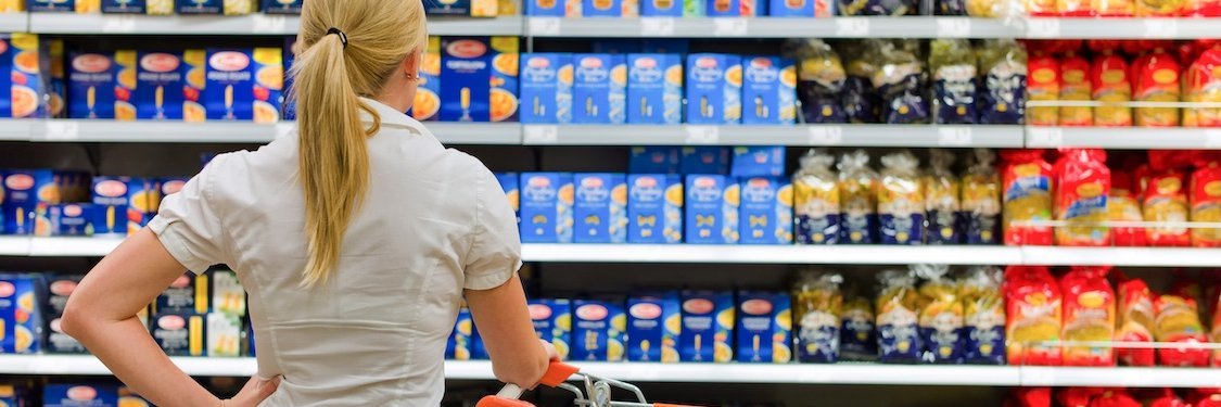Eine Frau mit einem Einkauswagen steht vor einem Supermarktregal.
