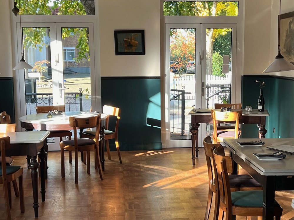 In einen Gastraum mit Holzparkett scheint die Sonne.