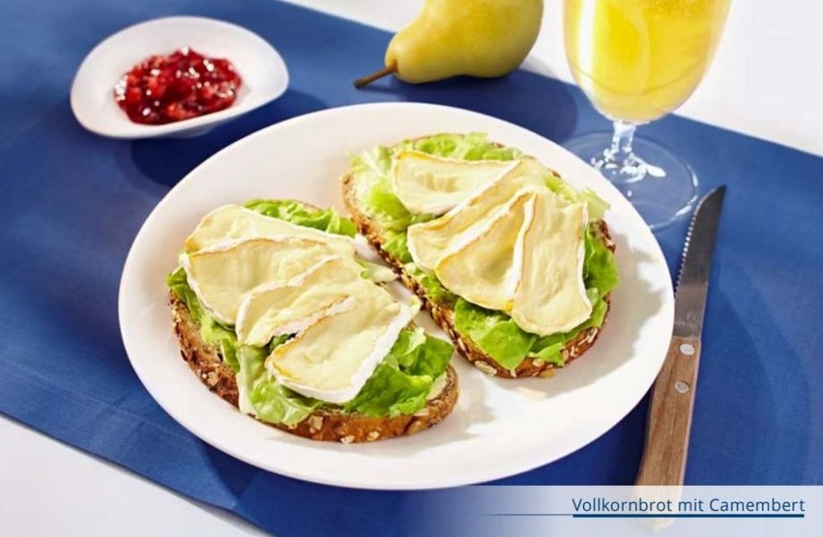 Zwei Brotscheiben mit Camembert auf Salatblatt und Schälchen mit Preiselbeeren.
