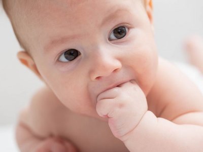 Ein auf dem Bauch liegendes und sich aufstützendes Baby hat seine Faust im Mund.