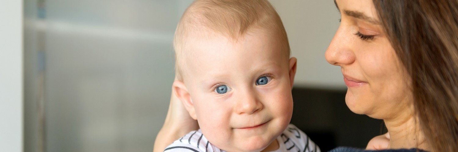 Eine Mutter hält ihr Baby von etwa sechs Monaten auf dem Arm. 