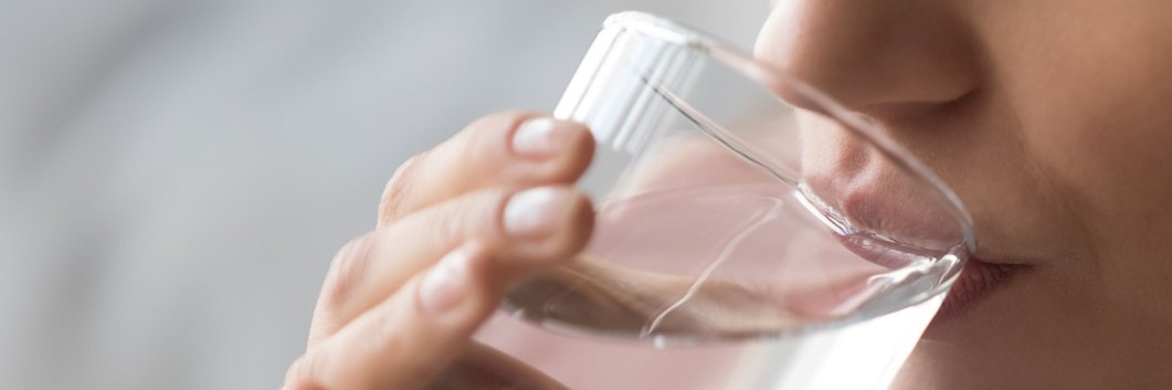 Eine Frau trinkt aus einem Glas mit Wasser.