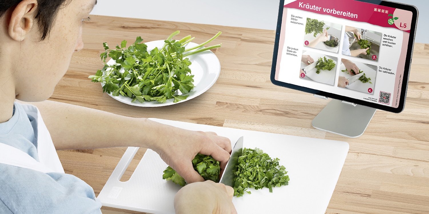 Ein Junge schnippelt Petersilie vor einem Tablet.. Artikel "Die Küchenkartei" öffnen.
