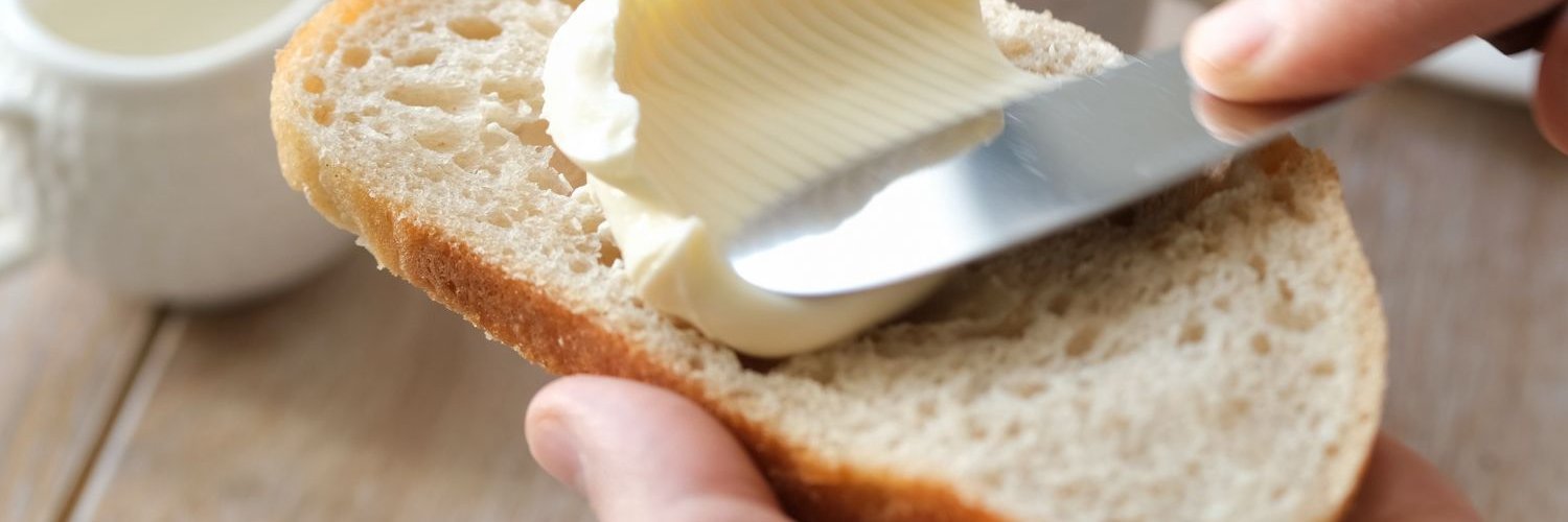 Eine Hand streicht mit einem Messer Butter auf eine Scheibe Brot. 