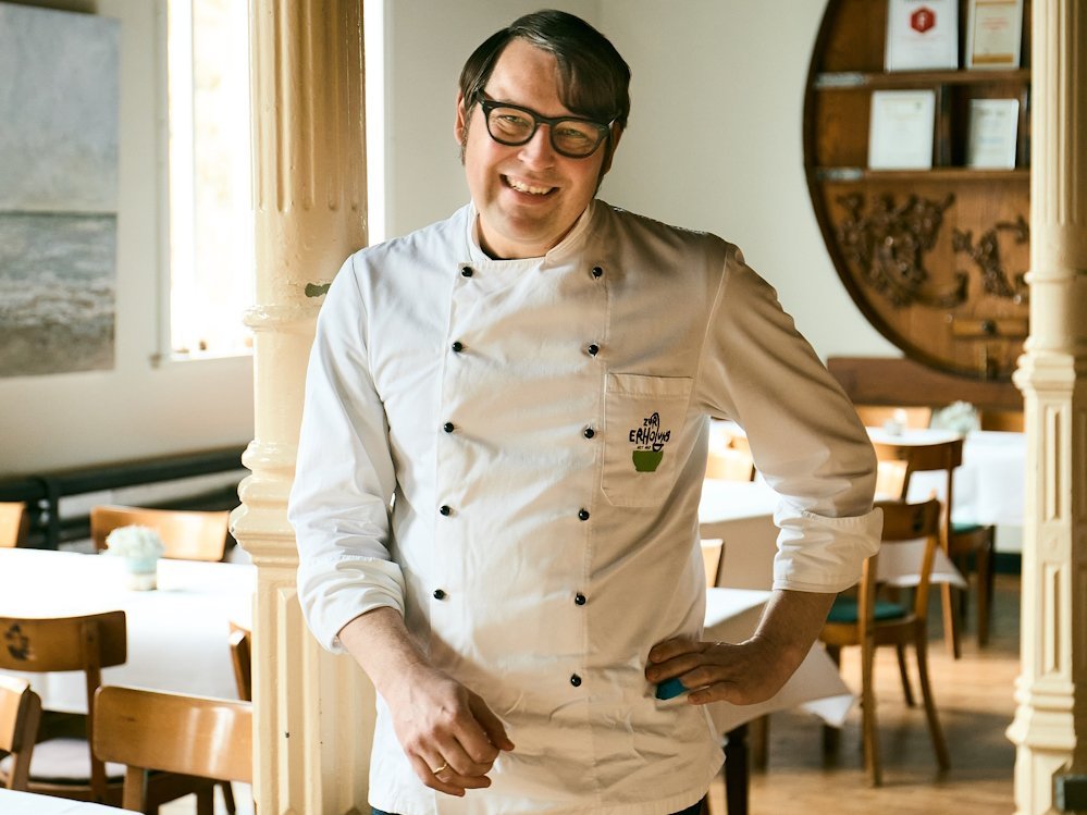 Portraet eines Mannes mit Kochjacke, der in die Kamera laechelt.