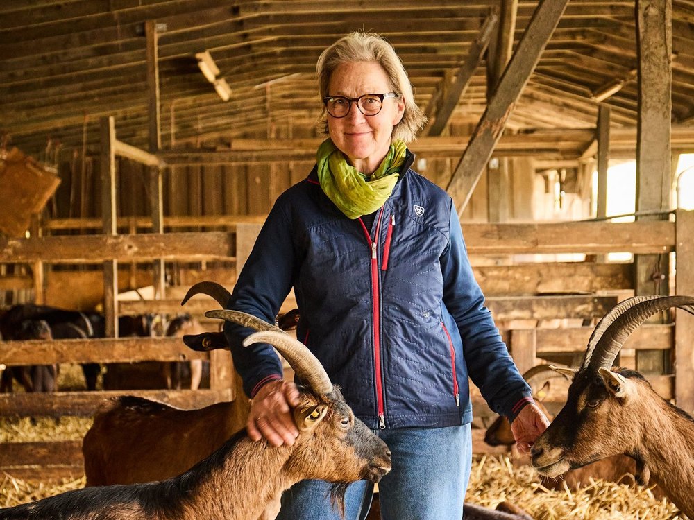 Eine Frau steht in einem Stall mit Ziegen.