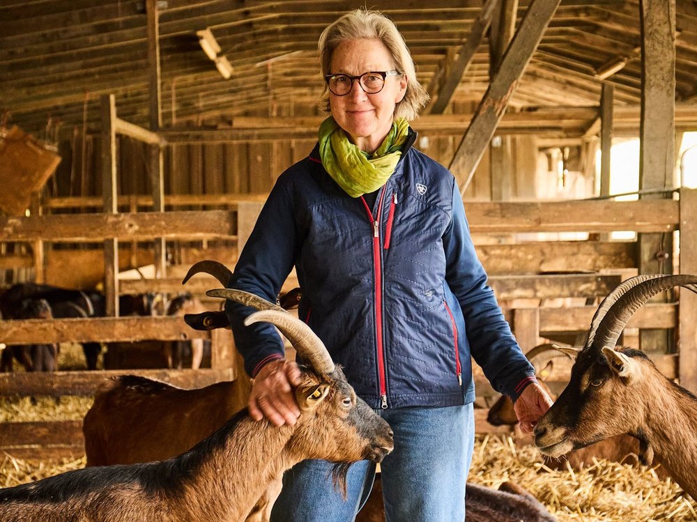 Eine Frau steht in einem Stall mit Ziegen.
