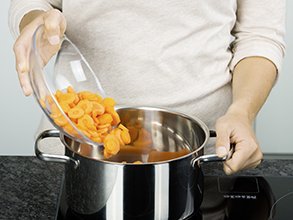 Eine Person gibt Möhrenscheiben in einen Topf.