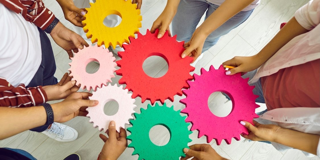 Hände von jungen Menschen verbinden bunte Zahnräder, die ineinander greifen.