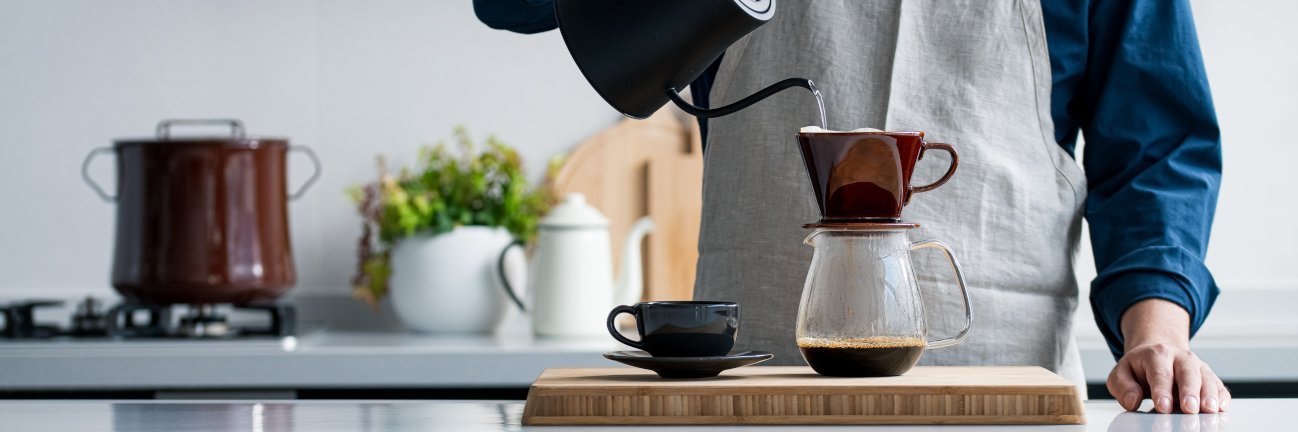 Ein Mann gießt Wasser aus einer Kanne in einen Handfilter für eine Tasse Kaffee.