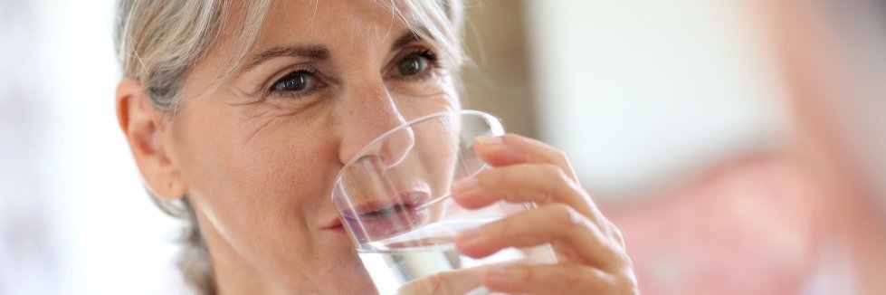 Eine ältere Frau trinkt ein Glas Wasser.