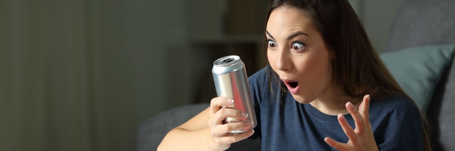 Mädchen hält Energydrink in der Hand und schaut entsetzt auf die Dose.