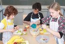 Drei Kinder schnoppeln Gemüse im Klassenzimmer