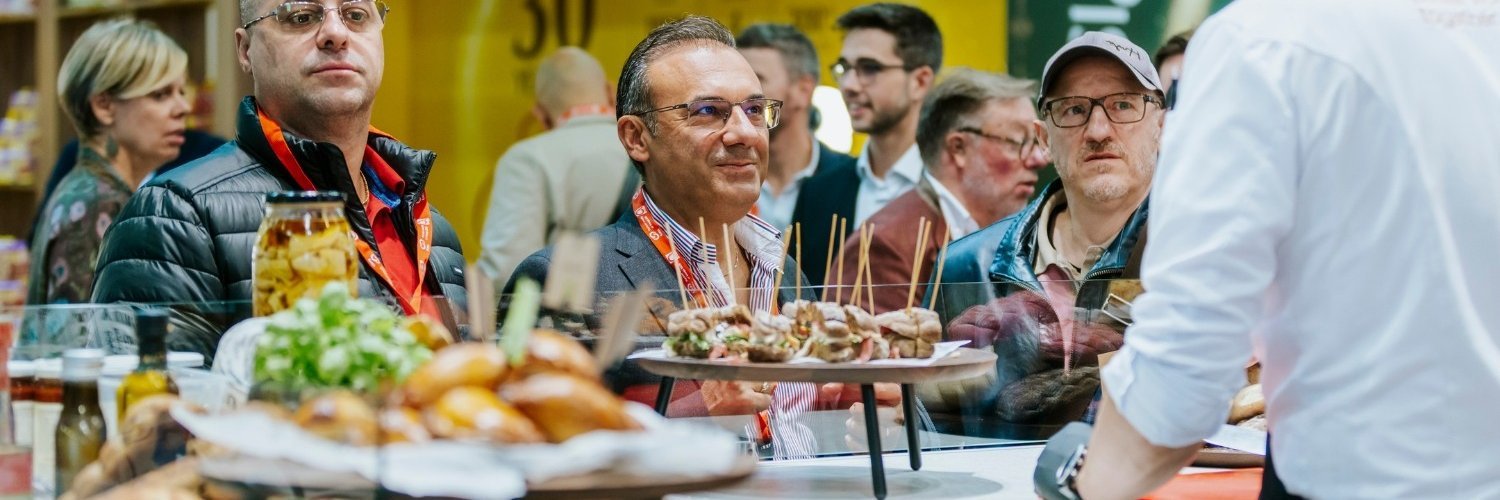 Besucherinnen und Besucher schauen sich einen Messestand mit Kostproben auf der Anuga an. 