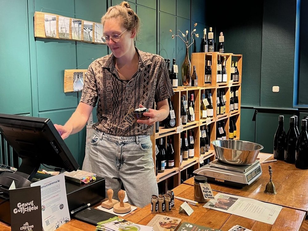 Eine Frau steht in einem Laden und tippt den Preis in eine Kasse ein.