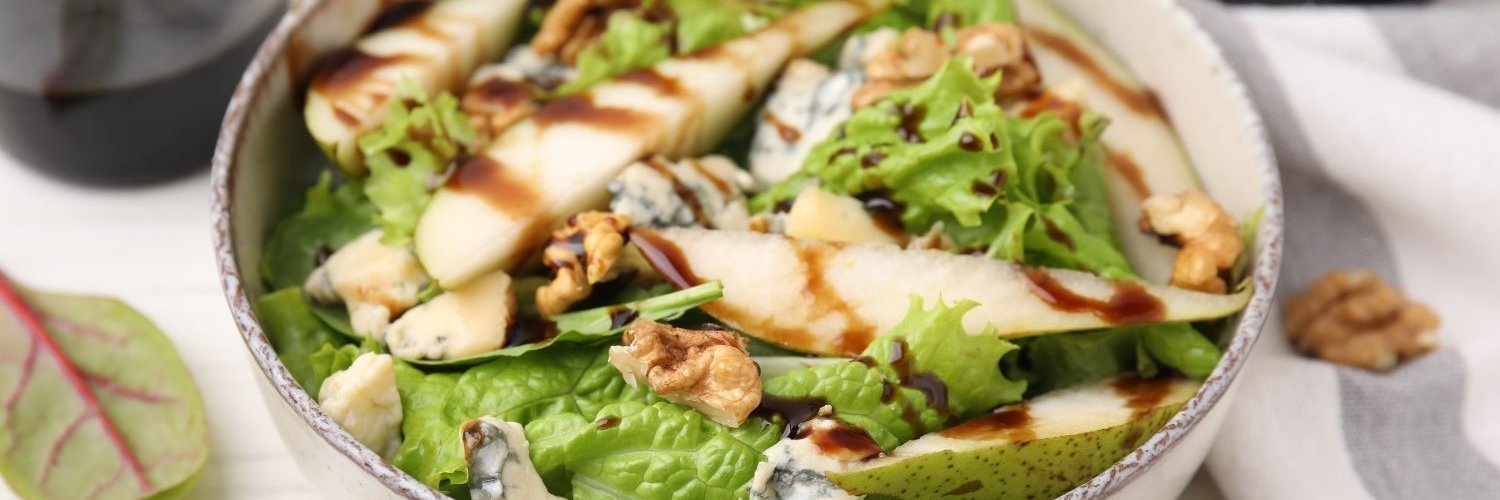 Eine Salatschüssel mit grünem Salat, Birnen, Walnüssen und Balsamico-Dressing. 