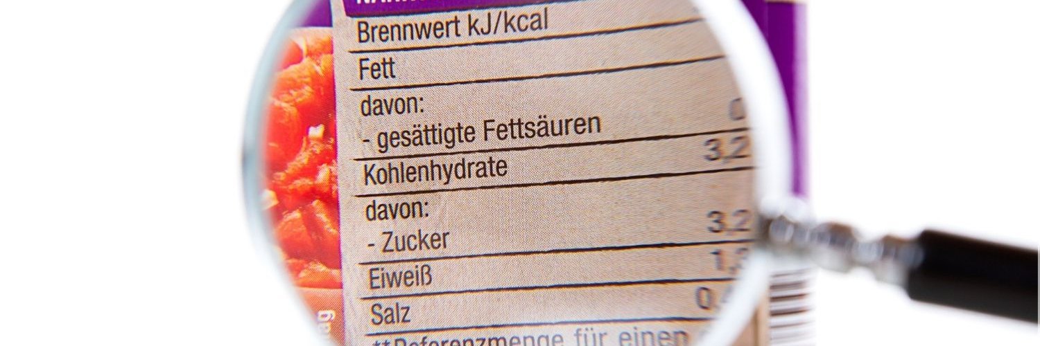 Durch eine Lupe wird die Kennzeichnung einer Konservendose vergrößert, sodass man die durchschnittlichen Nährwerte erkennen kann.