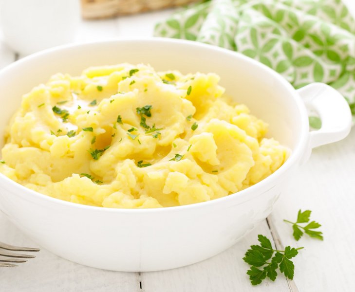Kartoffelpüree mit Petersiliengarnitur steht in einer weißen Schale auf dem Tisch.
