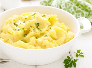 Kartoffelpüree mit Petersiliengarnitur steht in einer weißen Schale auf dem Tisch.