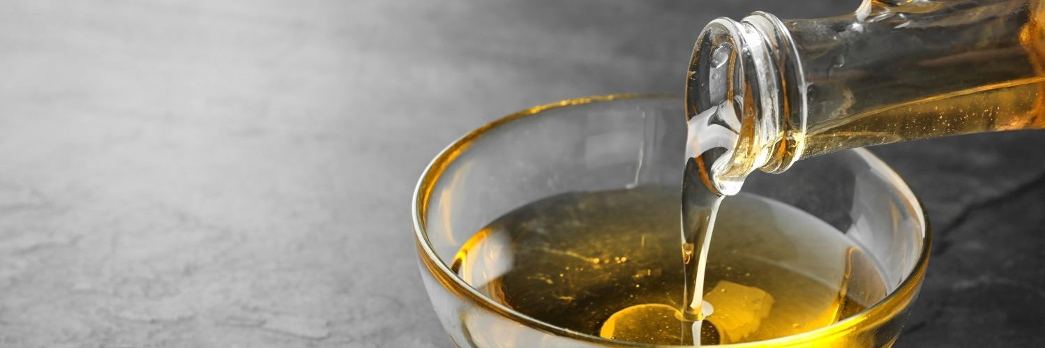 Aus einer Rapsölflasche wird goldgelbes Rapsöl in eine Glasschüssel gegossen.