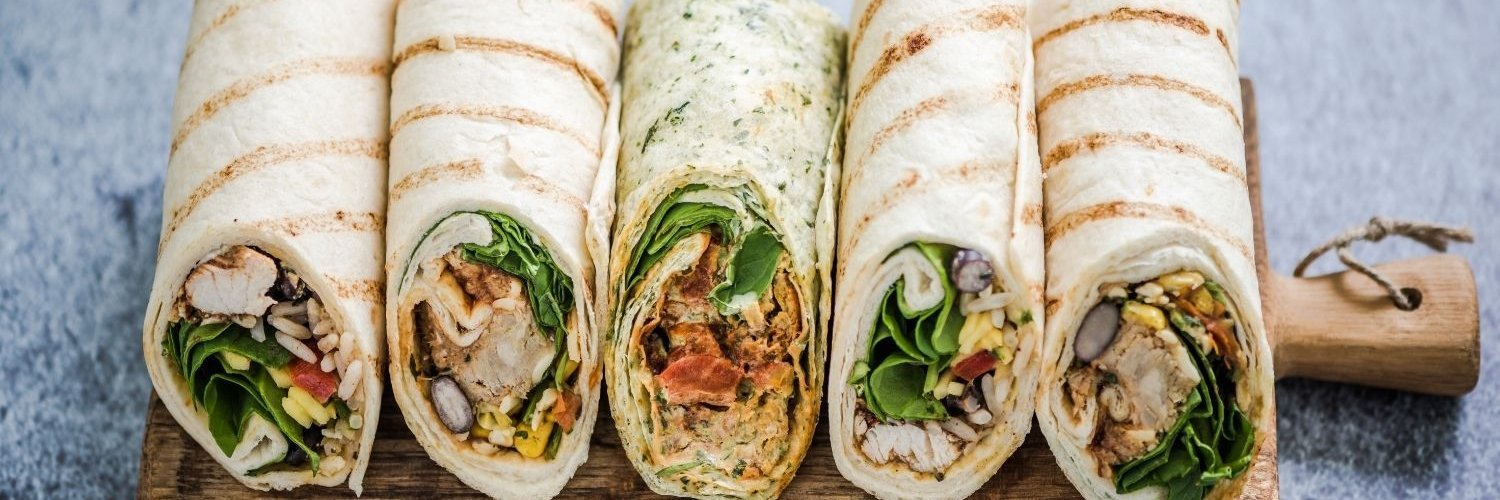 Auf einem Holzbrett liegen fünf Wraps nebeneinander, die unterschiedlich mit Salat, Gemüse, Fleisch und Reis gefüllt sind.