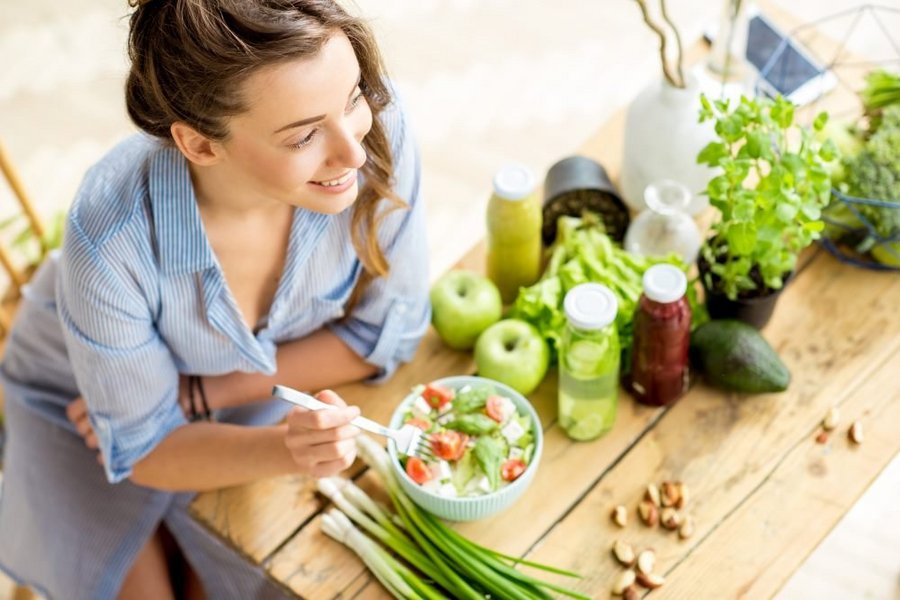 Frau steht an der Küchenarbeitsplatte und isst einen Salat aus einer Bowl. 