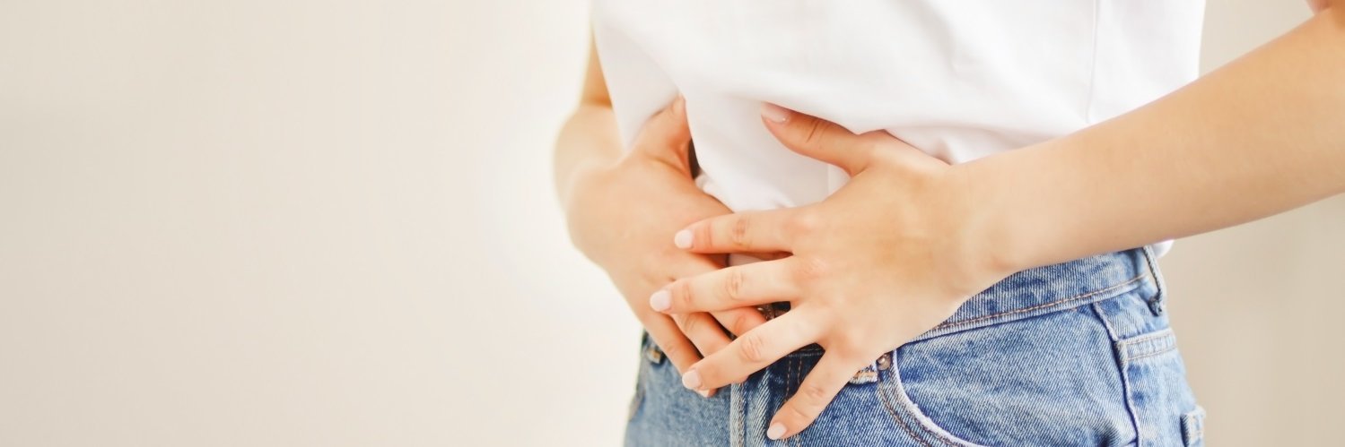 Eine Frau in Jeans und weißem T-Shirt drückt beide Hände auf ihren Bauch. 