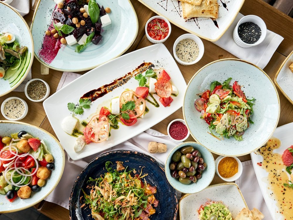 Mehrere weiße Teller und Schüsseln mit vegetarischen Speisen stehen durcheinander auf einem Tisch.