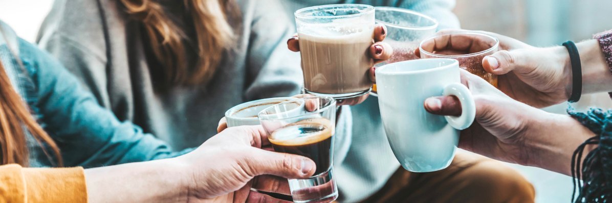 Mehrere Personen stoßen mit verschiedenen Kaffeetassen und Bechern an.