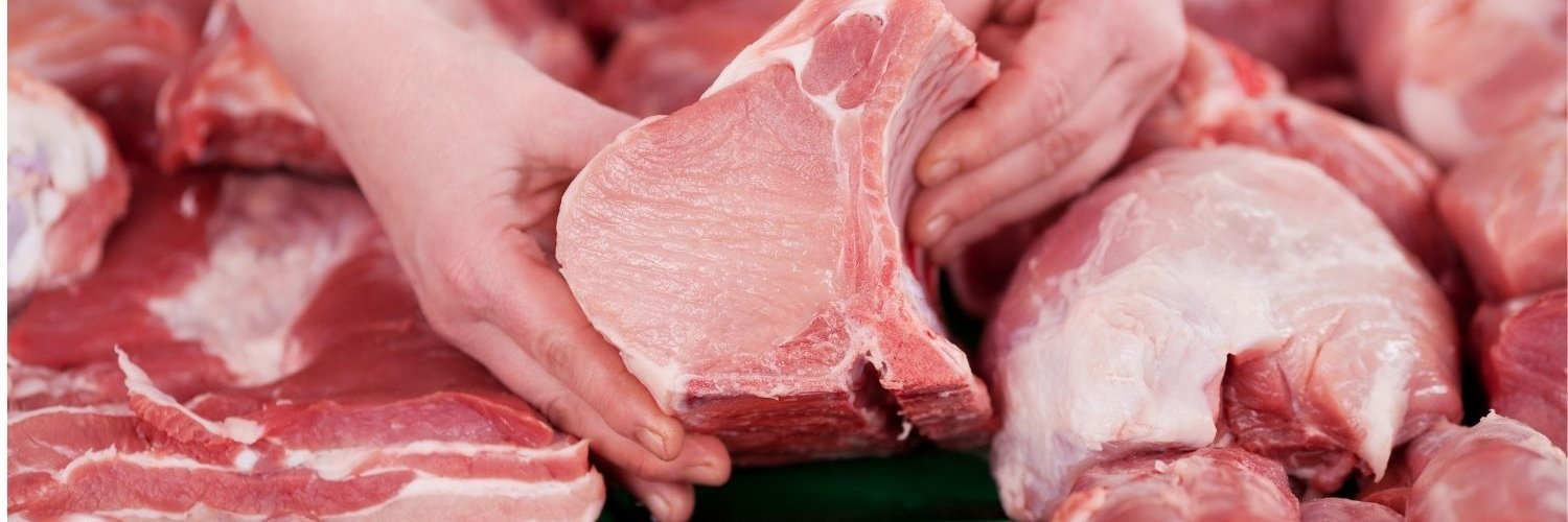 An einer Fleischtheke halten Hände ein Stück Schweinefleisch. 