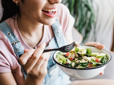 Eine Frau isst aus einer kleinen Schüssel einen bunten Salat.