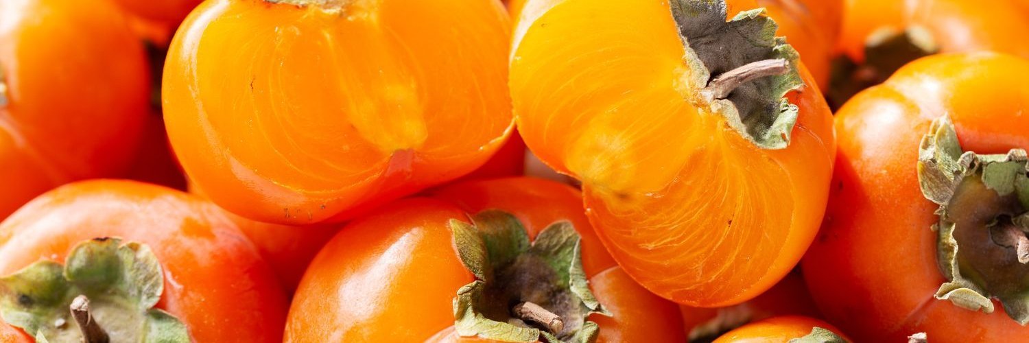 Das Bild ist ausgefüllt mit reifen Kaki der Sorte Persimone, einige sind aufgeschnitten.