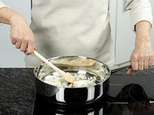 Eine Person dünstet Zwiebeln im Topf an.