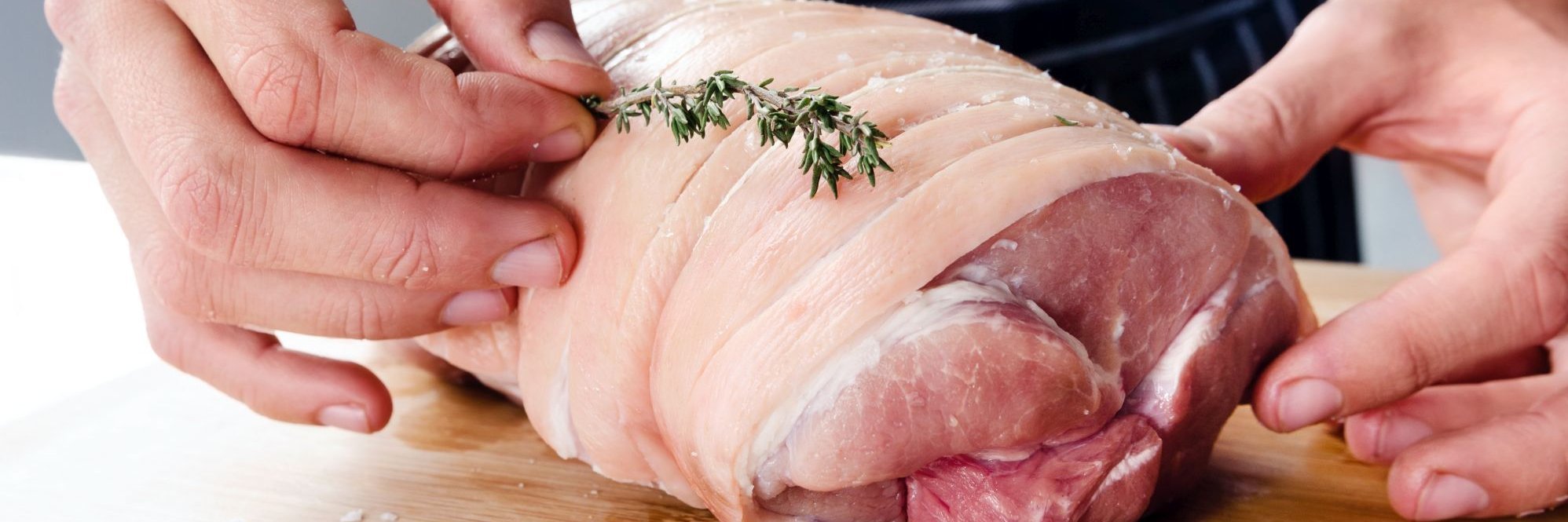 Männliche Hände befestigen einen Thymianzweig auf einem rohen Rollbraten vom Schwein.