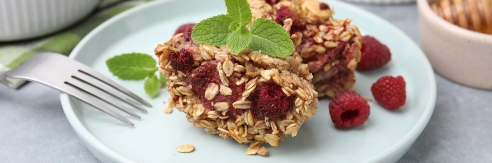 Auf einem weißen Teller liegt ein gebackene Haferflocken mit Himbeeren. 