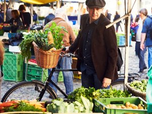 Ein Mann hält ein Fahrrad in der Hand und betrachtet das Angebot an einem Gemüsestand.