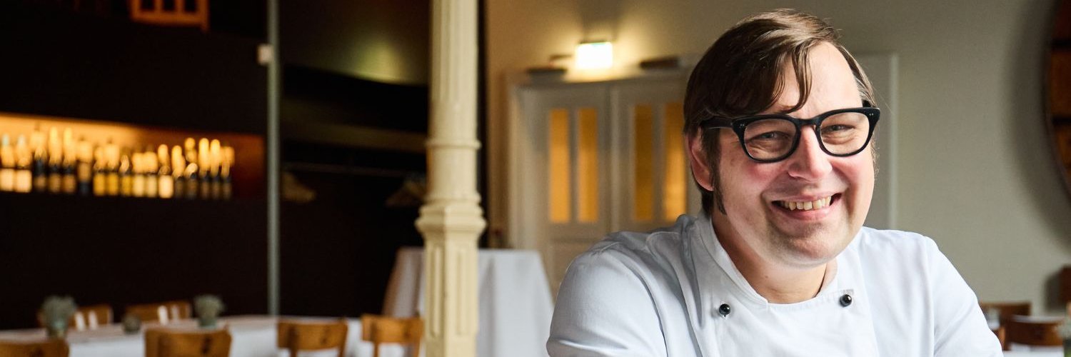 Koch Bernd Ratjen sitzt an einem Tisch im Gastraum seines Gasthofes.