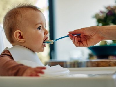 Ein Baby wird mit einem Löffel mit Brei gefüttert. 