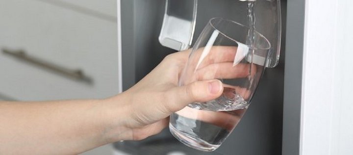 Eine Hand hält ein Glas, das an einem Wasserspender befüllt wird.  