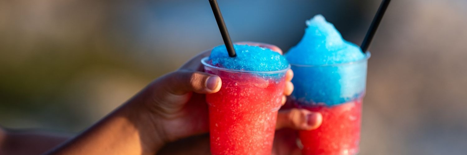 Zwei Hände halten zwei rot-blaue Slush-Eis-Getränke.