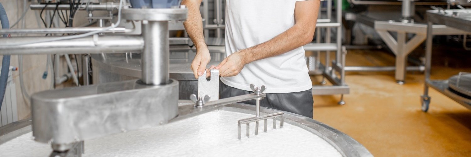Ein Mann mischt Milch im Edelstahltank während des Fermentationsprozesses bei der Käseherstellung