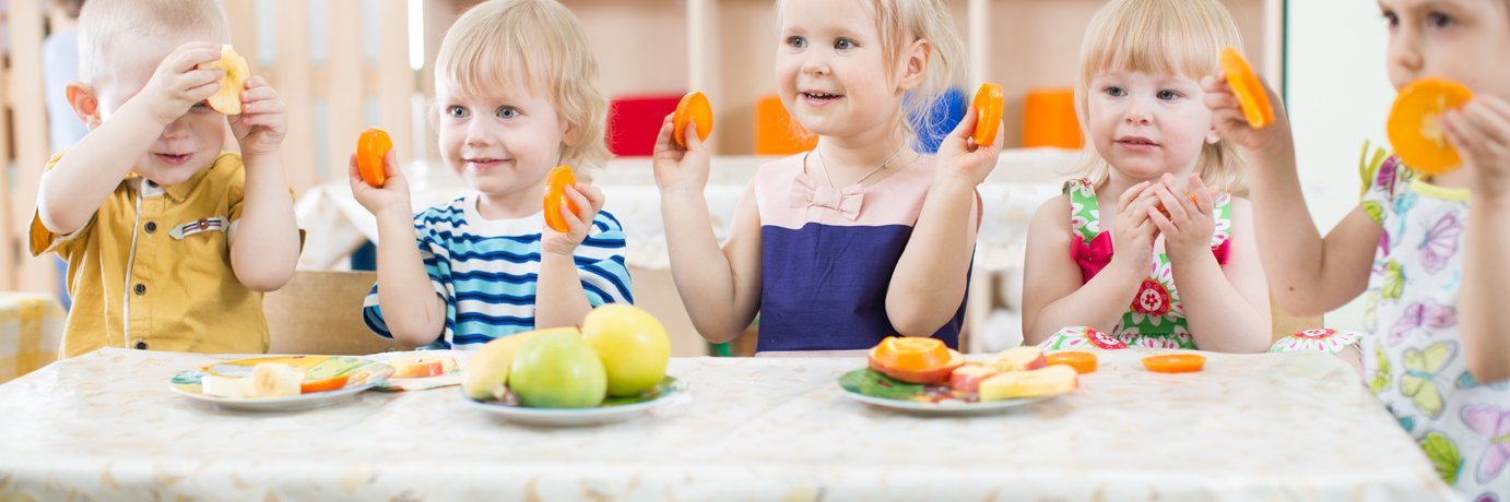 Kitakinder Sitzen an einem kleinen Tisch mit Tischdecke und essen geschnittenes Gemüse.