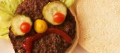 Trauriges Burger-Gesicht aus Brötchen, Hackfleisch, Gurken, Tomaten, Salat, Ketchup und Senf.