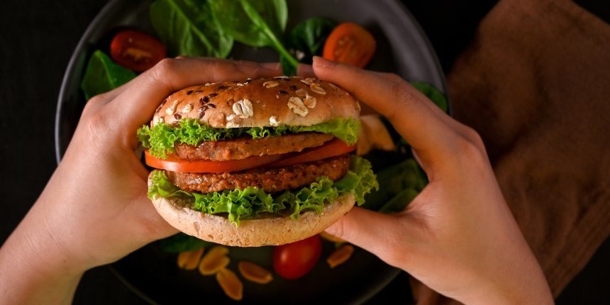 Zwei Hände halten einen vegetarischen Burger über einen Teller auf dem Salatblätter und Tomatenscheiben liegen.. Artikel "Vom Fast-Food zum Fit-Food" öffnen.