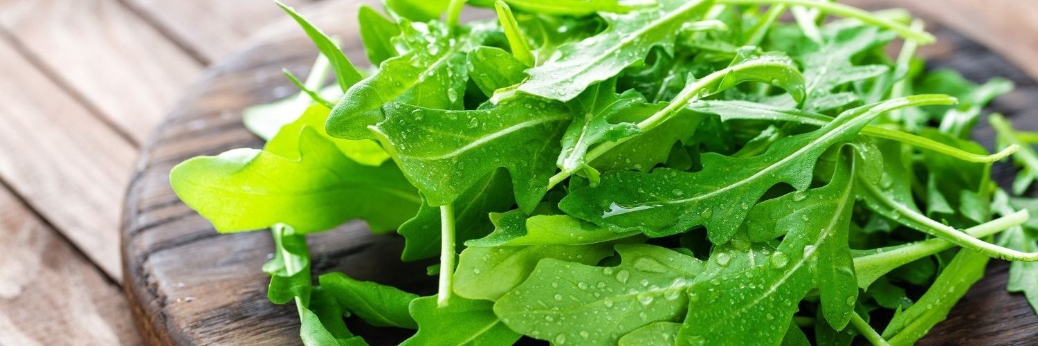 Auf einem Holzbrett liegt ein loser Bund frischer Rucolablätter.