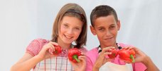 Zwei Kinder, die je eine Paprika und eine Tomate in den Händen halten.