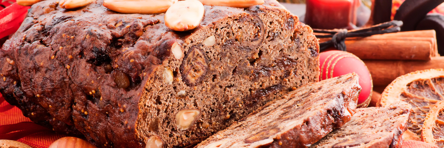 Ein Früchtebrot verziert mit Mandeln. Im Hintergrund liegt eine Weihnachtskugel und brennt eine Kerze. 