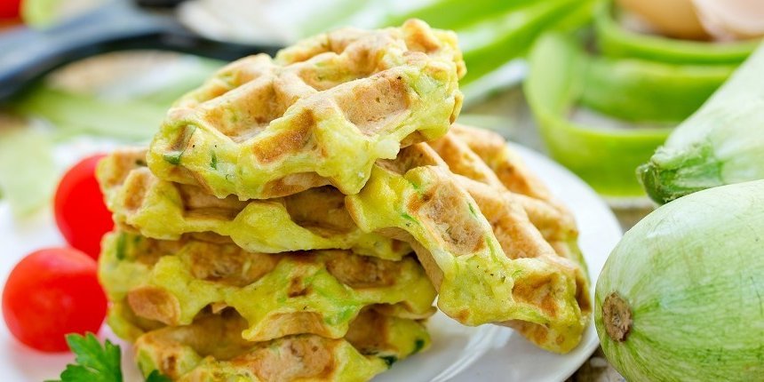 Auf einem Teller liegen mehrere Zucchini-Waffeln. Rechts daneben sind eine Zuchhini und kleine Tomaten. . Artikel "Herzhafte Waffeln für die schnelle Küche" öffnen.
