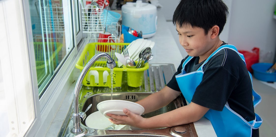 Ein Junge mit einer blauen Schürze spült Teller am Waschbecken ab.. Artikel "Hygiene beim pädagogischen Kochen" öffnen.